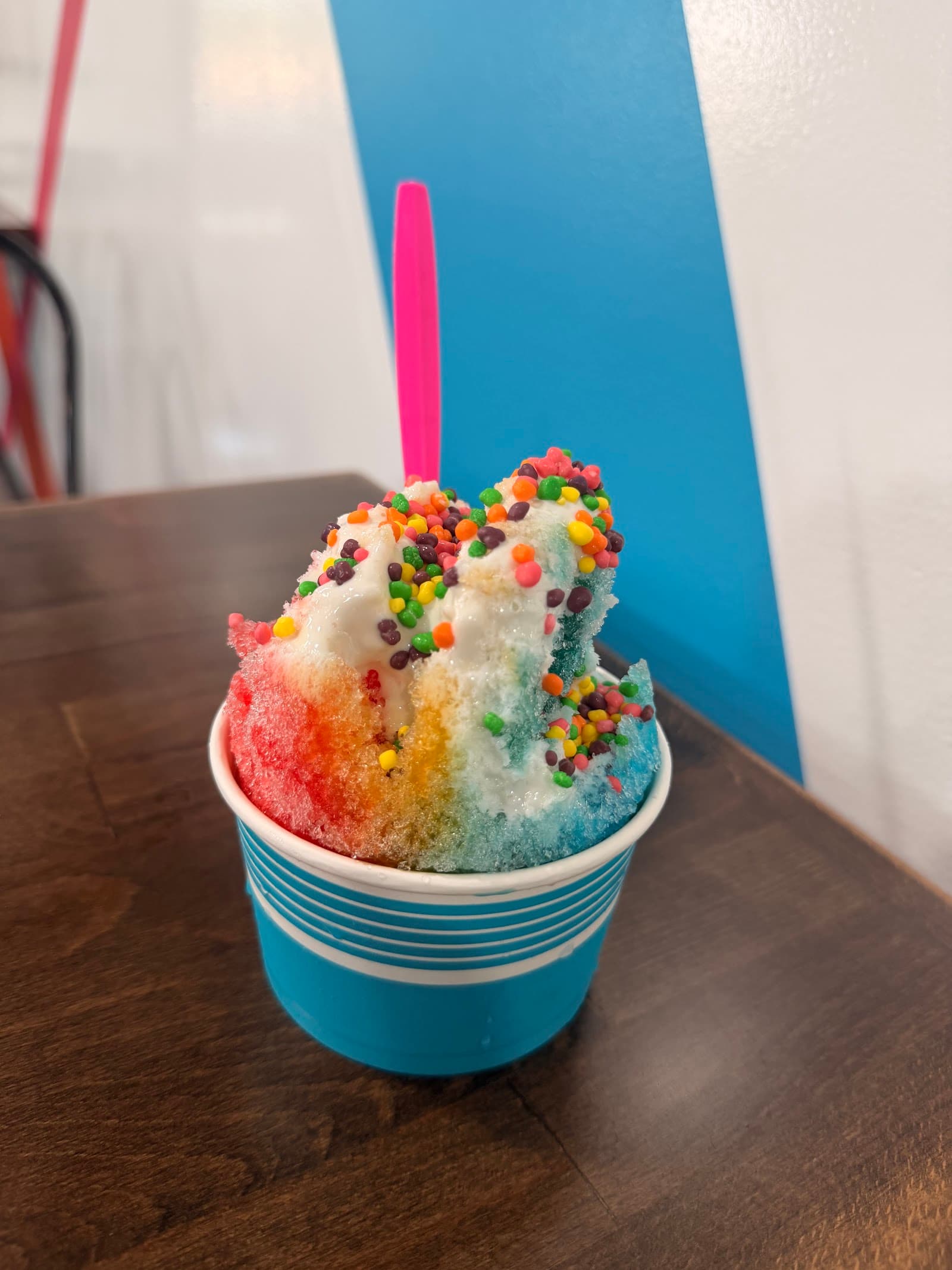 A rainbow Just Chillin snowball topped with cream and candy, with a pink spoon