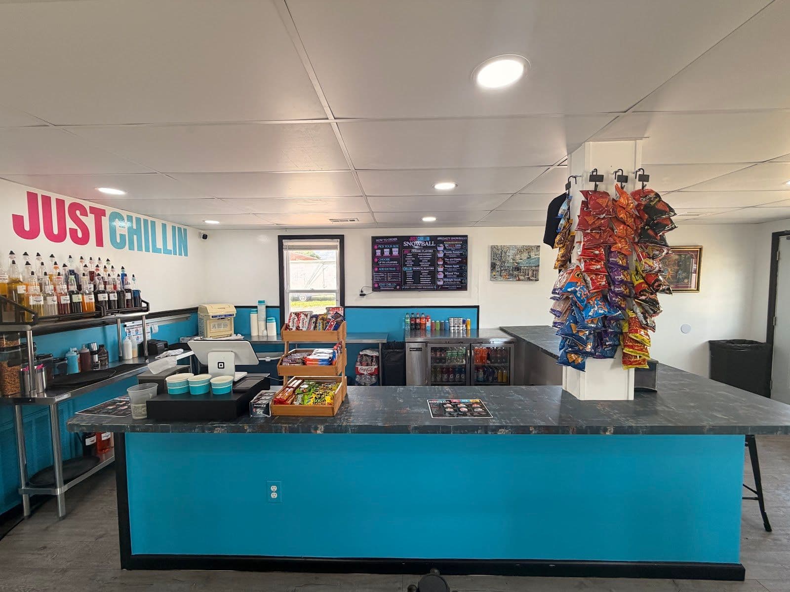 The service counter at Just Chillin Snowballs, with the painted logo, flavor syrups, and menu board