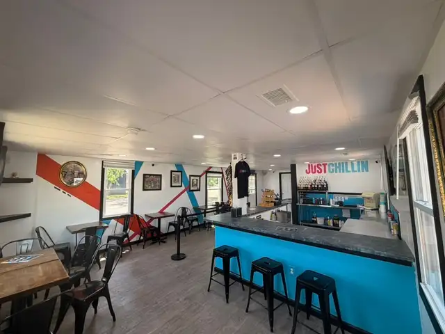 Inside Just Chillin in Glen Burnie: the Just Chillin sign above shelves of flavor syrup bottles, stools at the bright blue counter, and tables along the red and blue striped mural wall